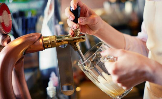 a woman pouring beer from tap into a pint glass